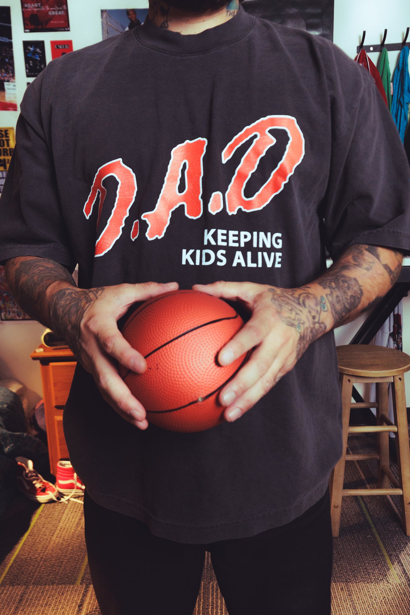 A person wearing a black oversized t-shirt with 'D.A.D Keeping Kids Alive" on the design.