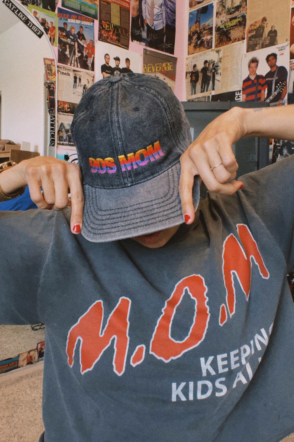 Person wearing a cap and t-shirt with text, standing in a room with posters on the wall.