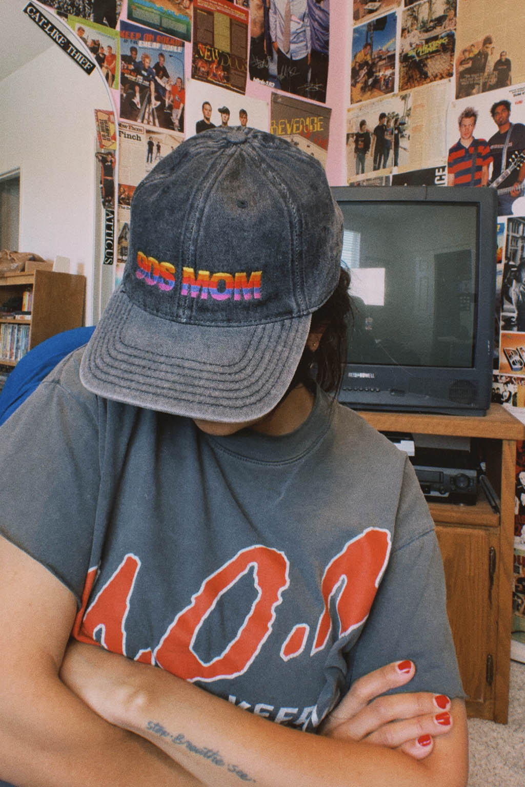 Person wearing a cap and t-shirt with colorful text in a room with posters on the wall.