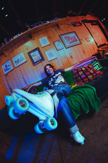Person sitting on a couch with glowing roller skates in a room with wooden walls and framed pictures.