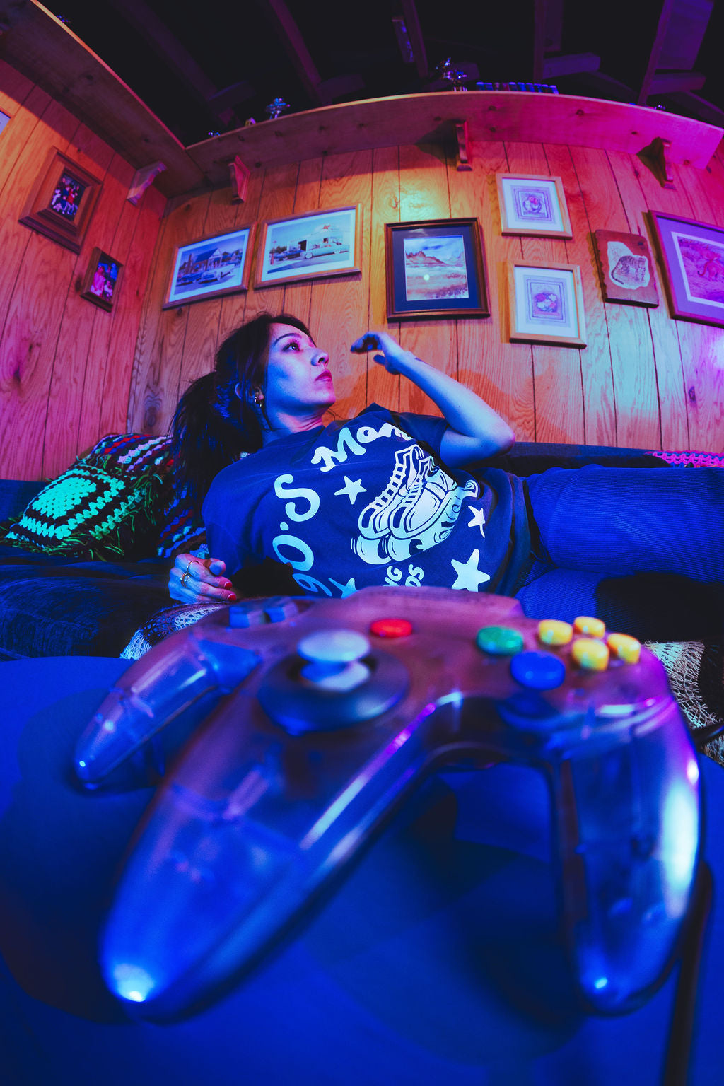 Person playing video games in a room with wooden walls and framed pictures.