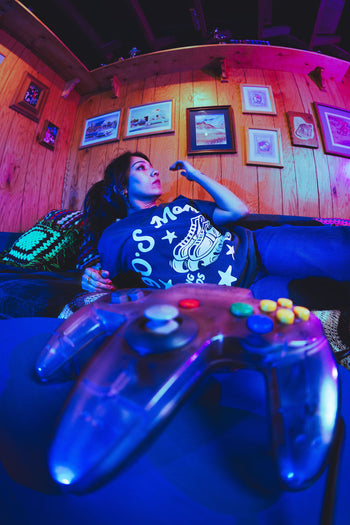 Person playing video games in a room with wooden walls and framed pictures.
