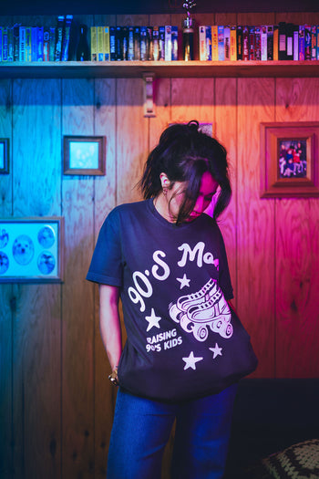 Person wearing a black t-shirt with white text and graphics in a room with colorful lighting.