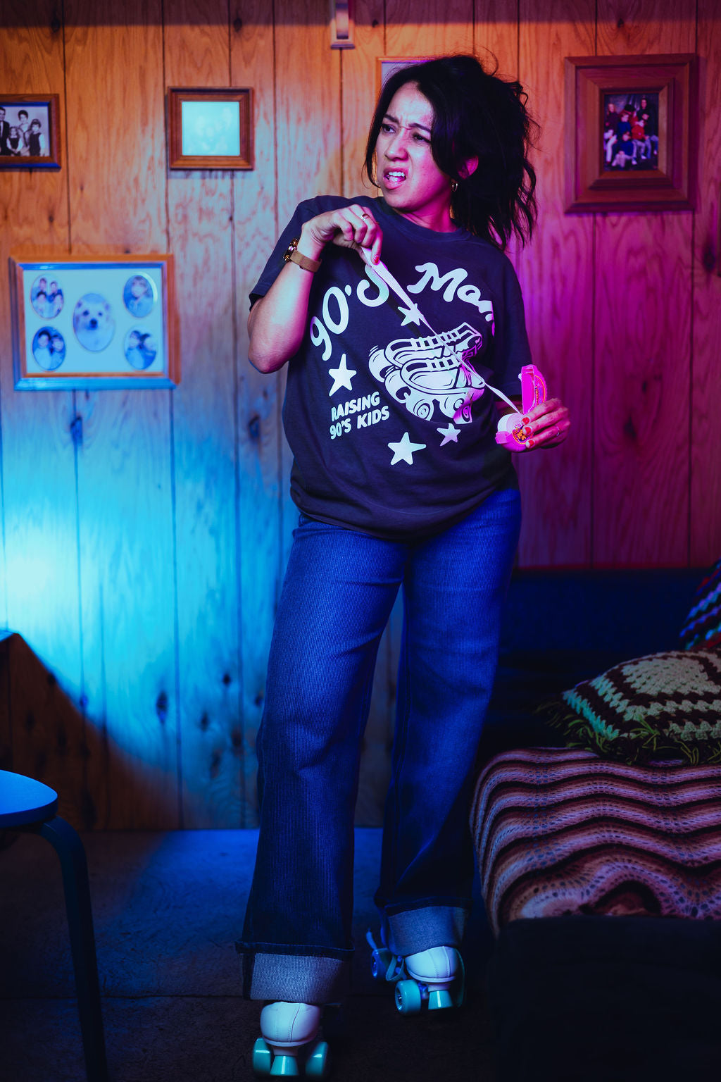 Person wearing a graphic t-shirt in a room with wooden walls and framed pictures.