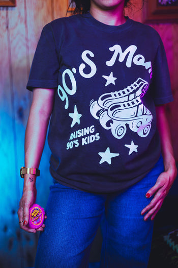 Person wearing a navy blue t-shirt with '90's Mom' graphic design, holding a pink object.