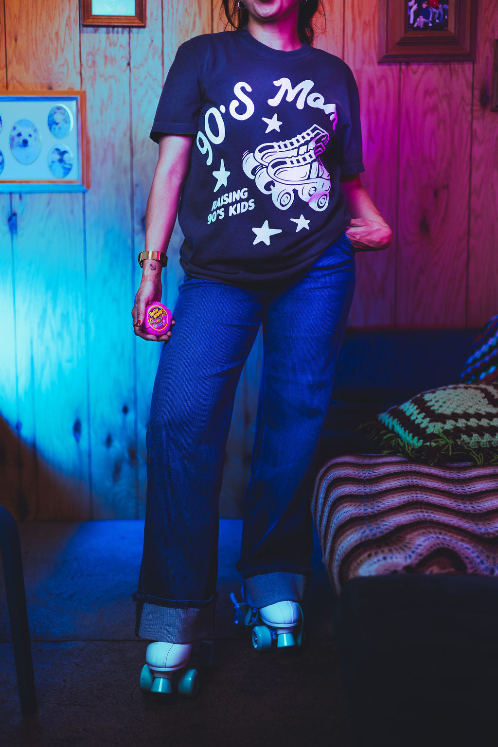 Person wearing a '90s Mom' t-shirt in a room with wooden walls and a bed.