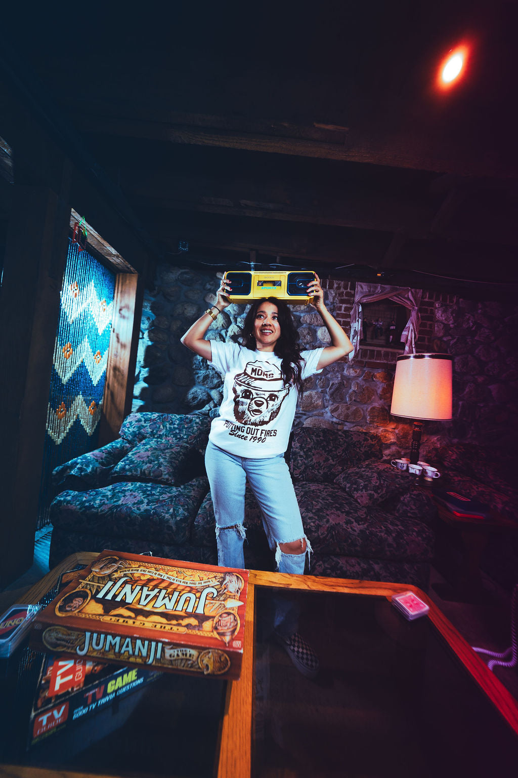 Person holding a skateboard above their head in a dimly lit room with a Jumanji game box on a table.